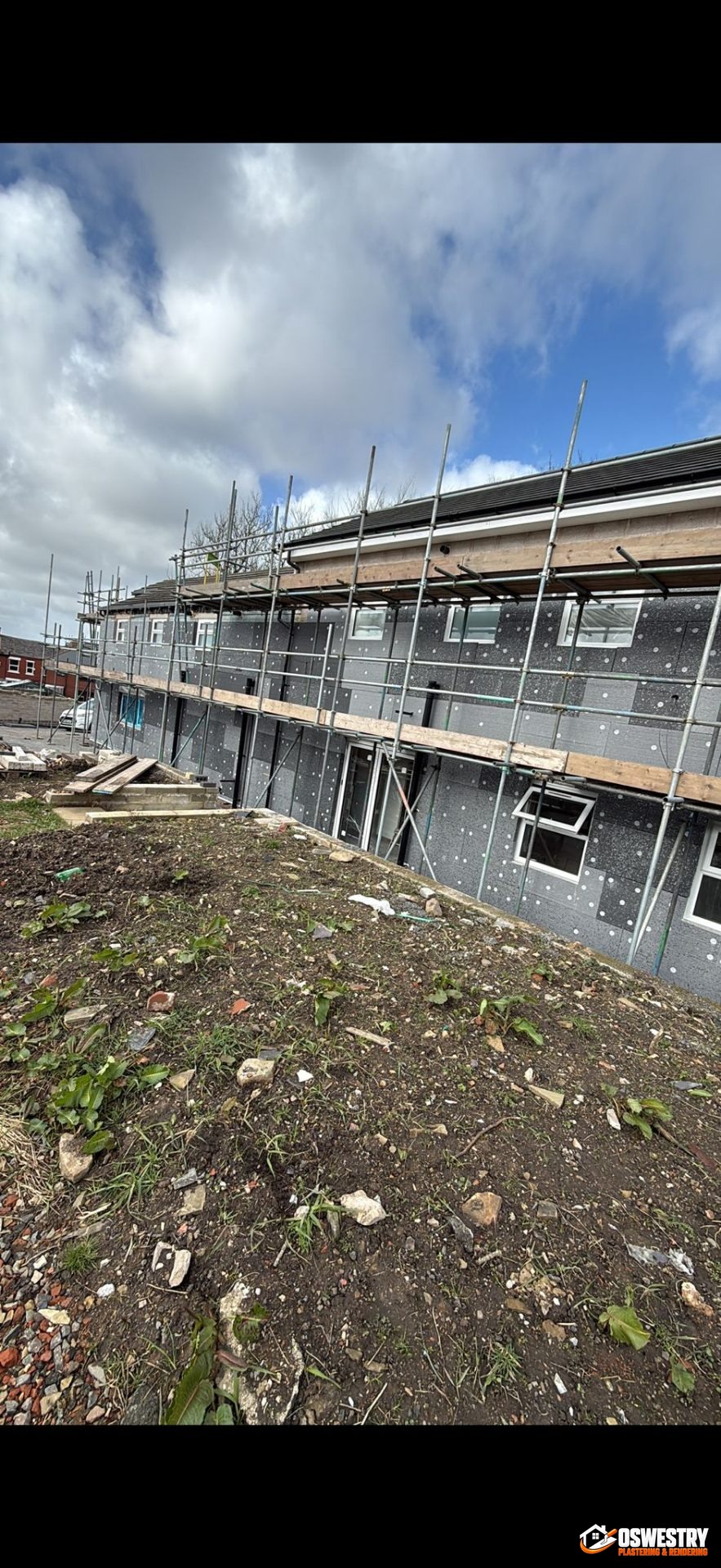 External Wall Insulation system mid-installation on a UK property — grey EPS insulation boards fixed and mechanically pinned across the elevation, scaffold in place ready for base coat and render